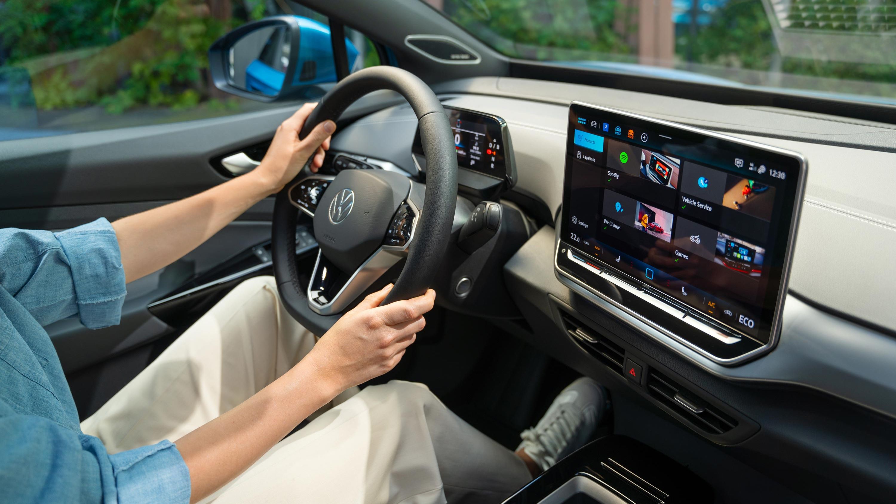 Lenkrad und Infotainment-System im VW ID.4, eine Frau sitzt auf dem Fahrersitz.