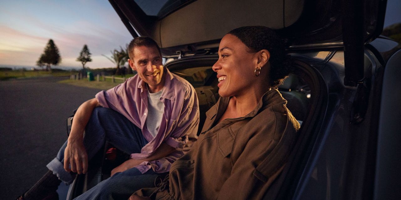 Ein Mann und eine Frau sitzen unter der geöffneten Heckklappe eines Volkswagen ID.7 Tourers