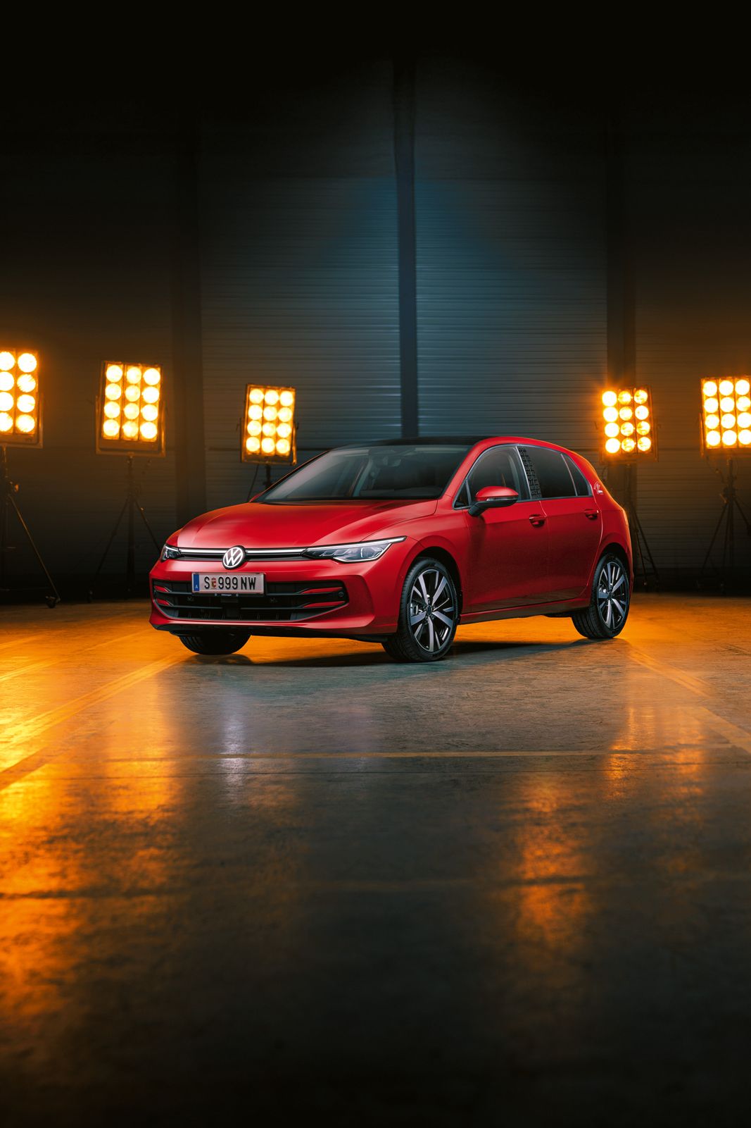 Ein roter Der VW Golf Falco Edition steht einer leeren Halle, dahinter Bühnenlicht.