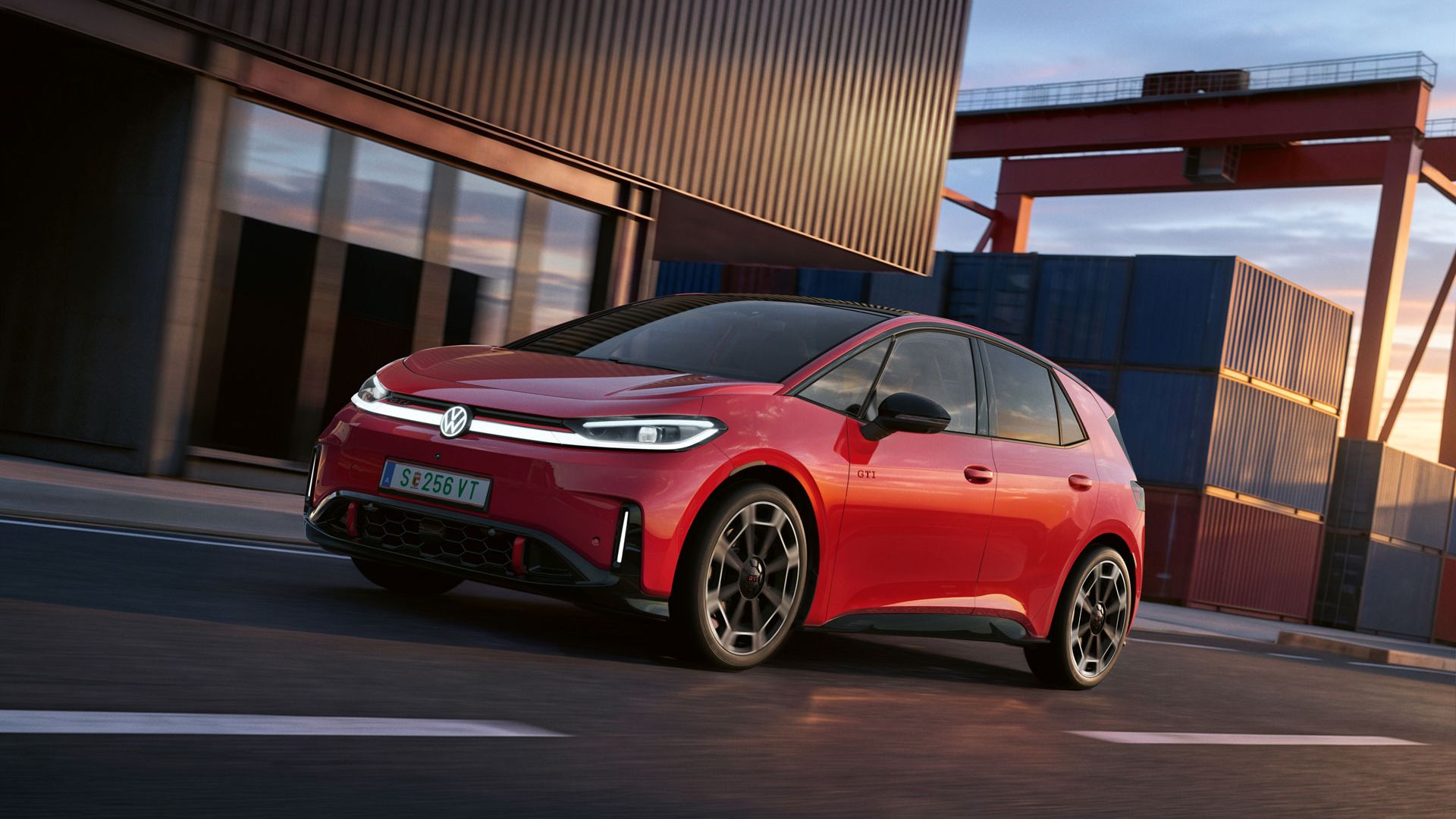 [AI-modified] – Ein roter VW ID.3 GTI fährt mit eingeschalteten Scheinwerfern und beleuchtetem Logo an einem Hafengebäude vorbei.