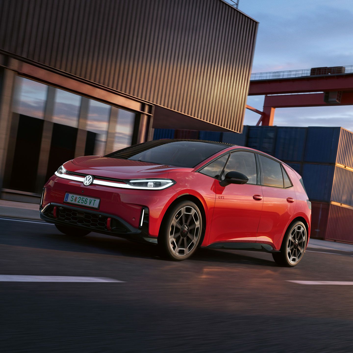 [AI-modified] – Ein roter VW ID.3 GTI fährt mit eingeschalteten Scheinwerfern und beleuchtetem Logo an einem Hafengebäude vorbei.