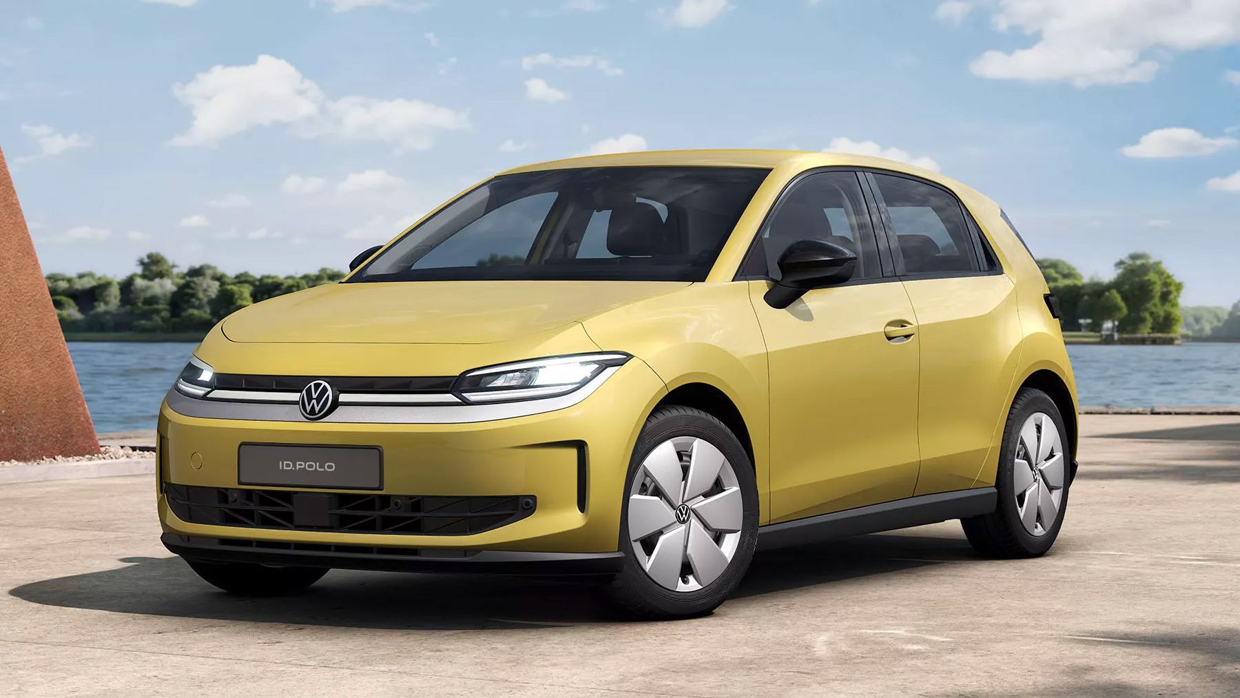 Ein gelber VW ID. Polo Trend von schräg vorne steht auf einem hellen Weg vor einem See.