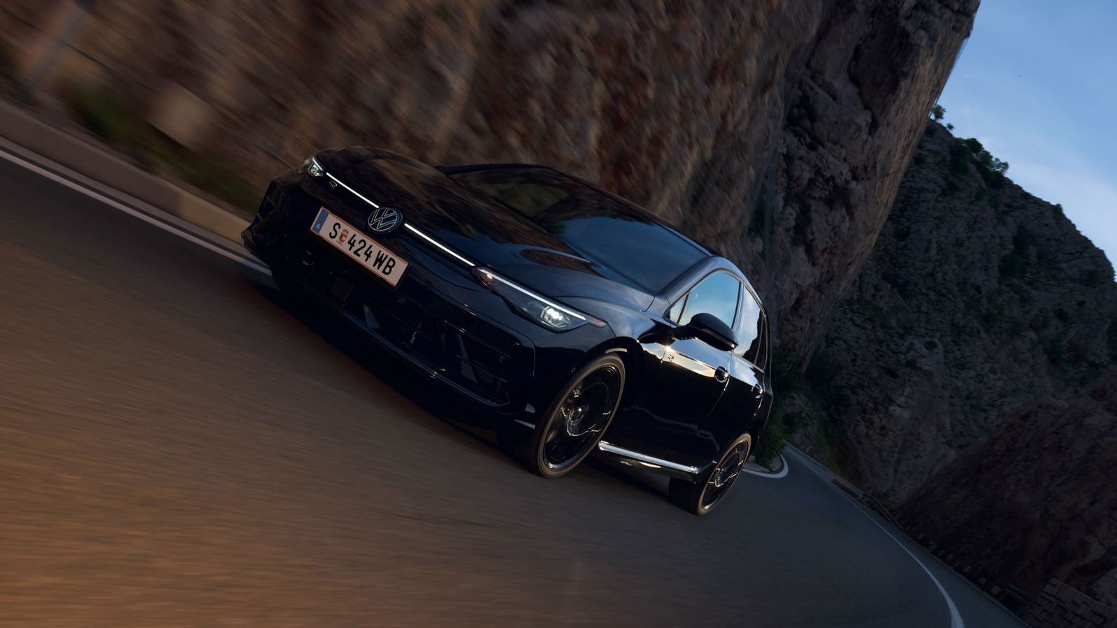 Golf R fährt auf einer Landstraße neben einem Berg.
