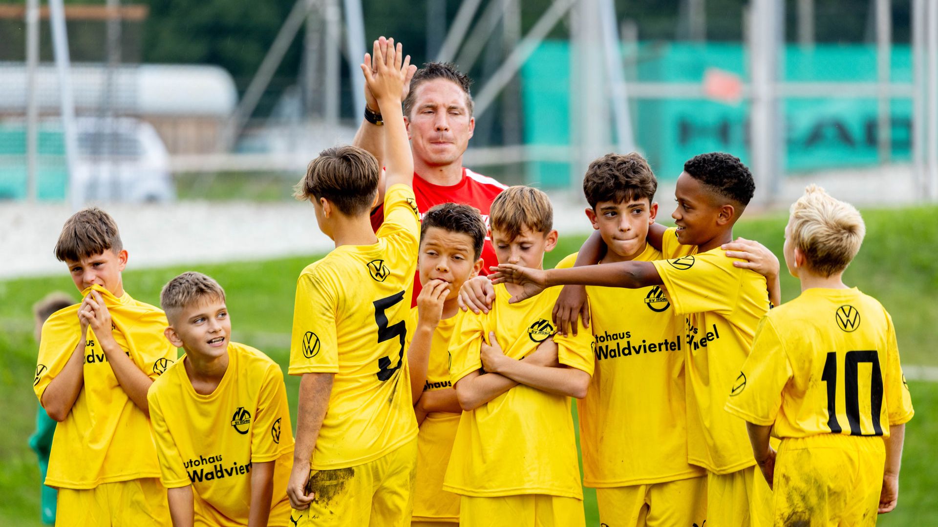 Die jungen Spieler eines Jugend-Fußballteams sammeln sich um ihren Trainer, ein Spieler gibt dem Trainer ein High Five