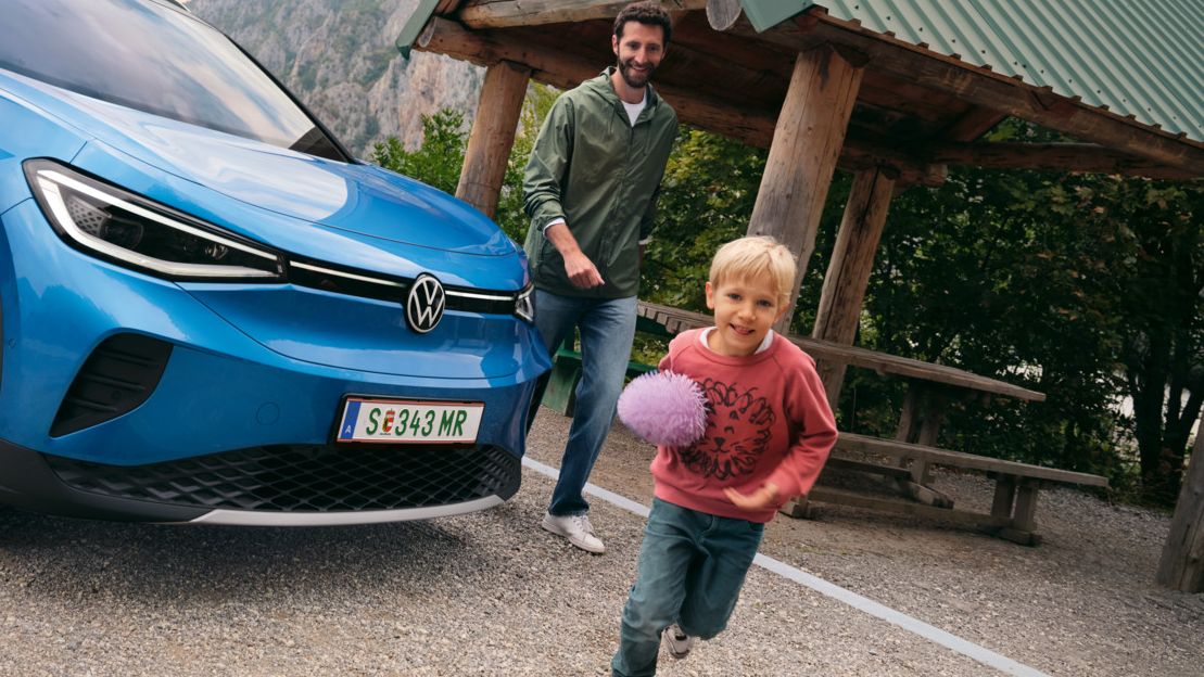 Vater und Sohn spielen mit einem Ball, daneben steht ein blauer VW ID.4.