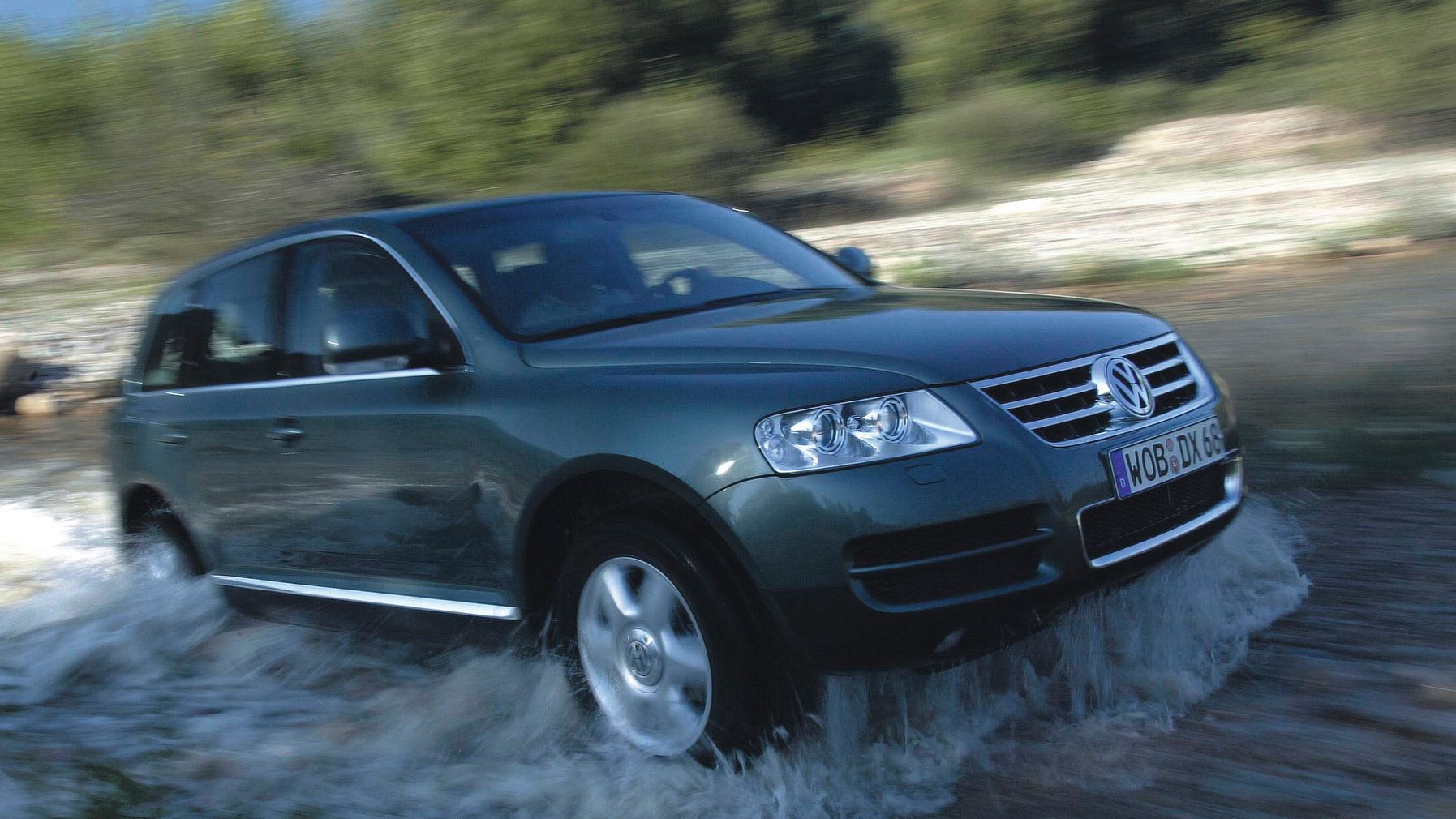 Ein dunkelgrüner VW Touareg fährt durch ein seichtes Gewässer.