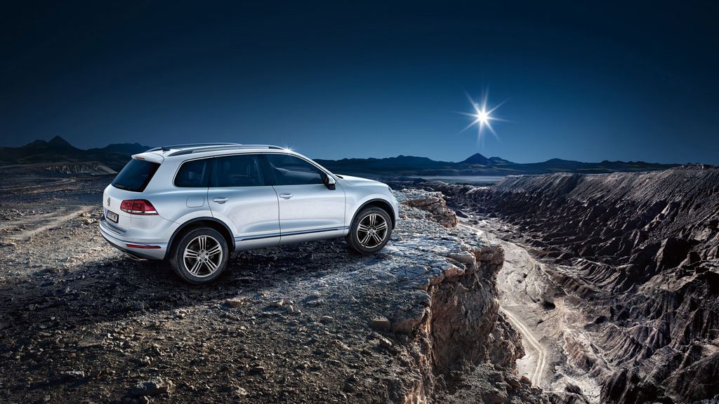 Ein VW Touareg Vorgängermodell steht an einer Klippe. Dahinter sieht man die Sonne 