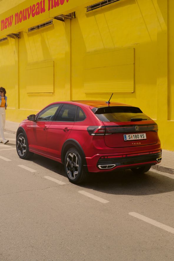 Ein roter VW Taigo steht vor einer gelben Halle am Straßenrand, eine Frau geht darauf zu.