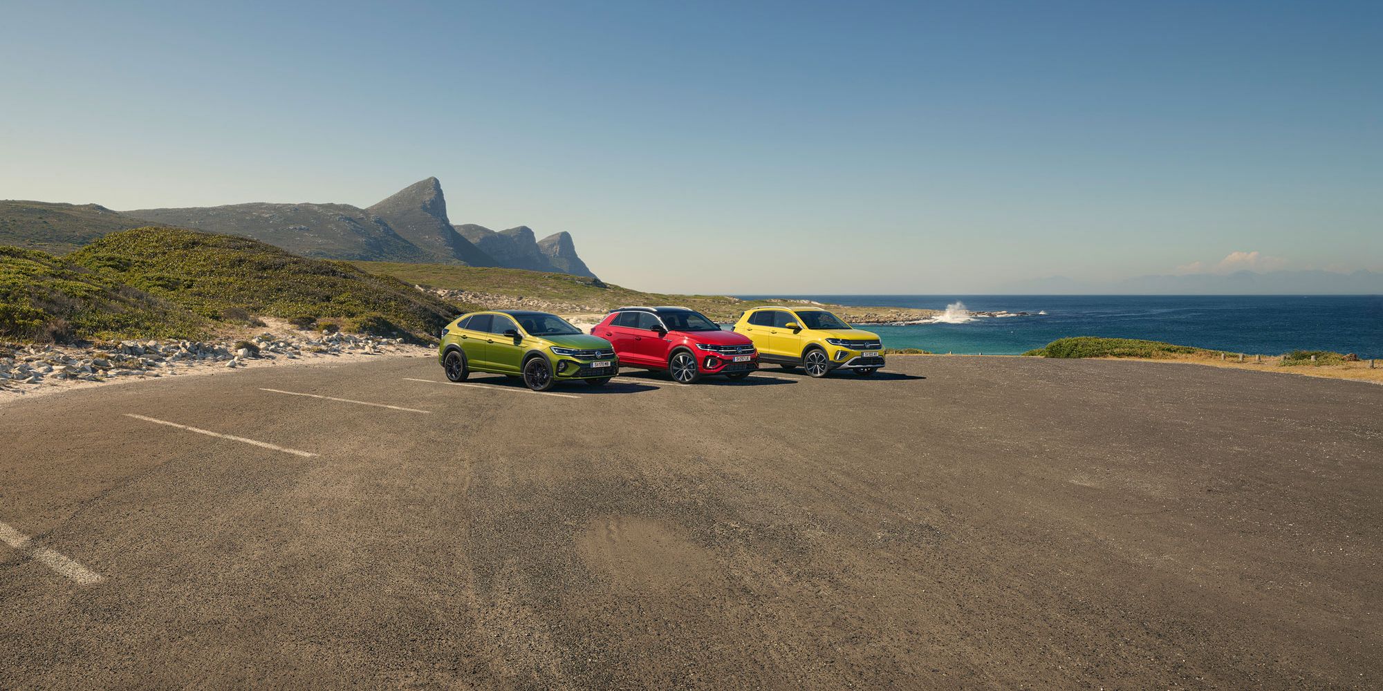 Taigo, T-Roc, T-Cross stehen geparkt auf einem Parkgelände, im Hintergrund sieht man das Meer.