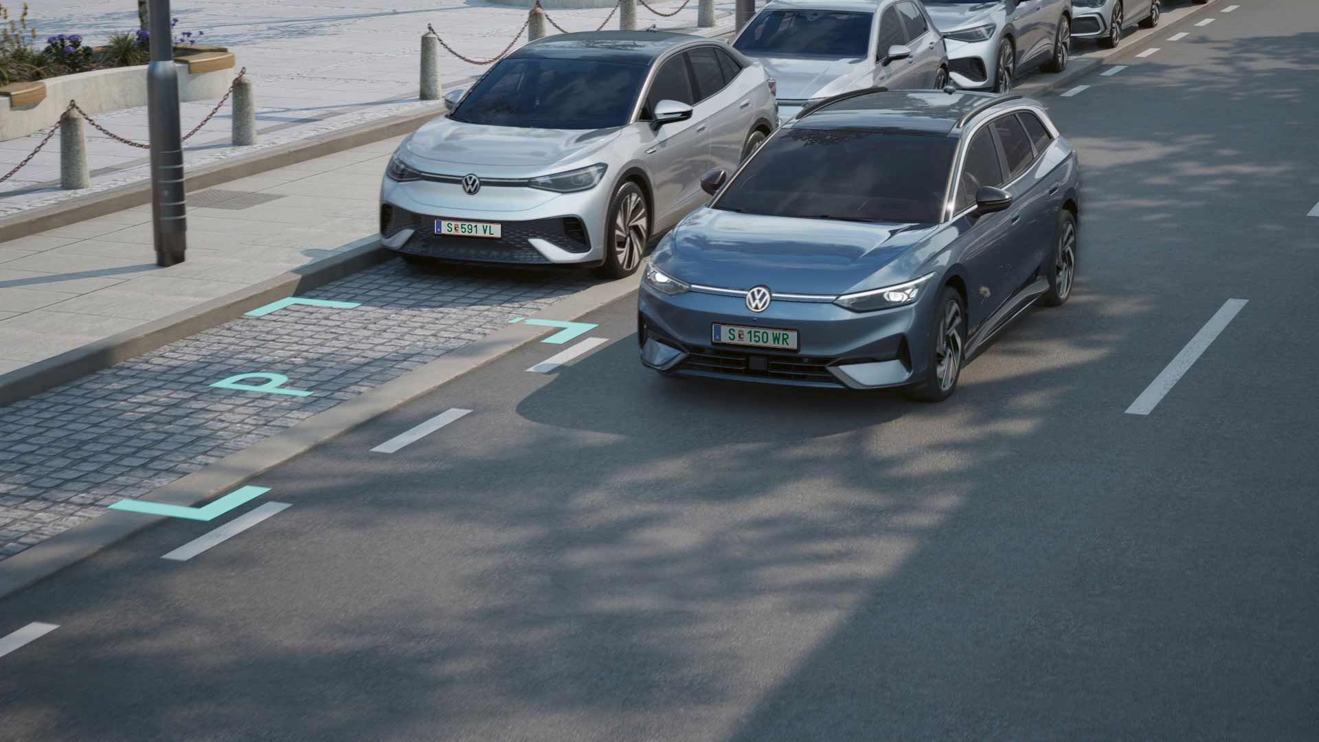 Zwei Volkswagen-Fahrzeuge, ein silberfarbenes und ein blaues, fahren selbstständig und parken vor einem Bürgersteig. Der Bürgersteig hat Absperrungen und Bänke. Es ist eine sonnige Tageszeit.