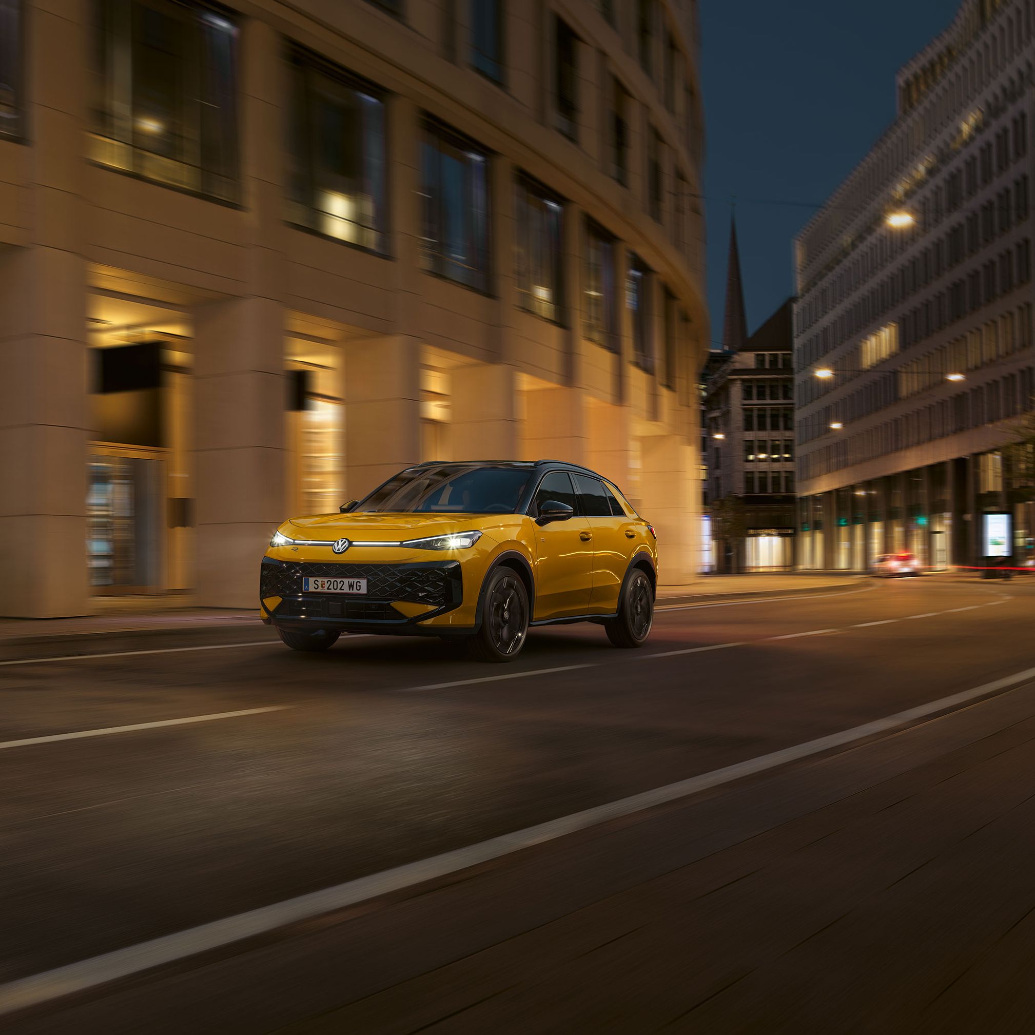 Ein gelber VW T-Roc R-Line fährt nachts durch eine urbane Umgebung.