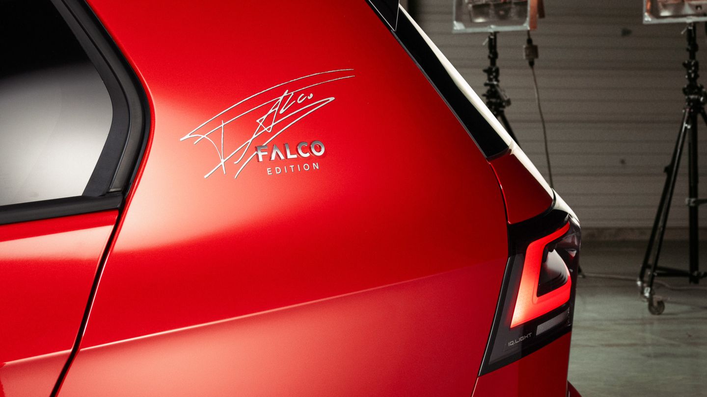 Detailaufnahme des Hecks eines roten VW Golf Falco Edition. Auf der C-Säule ist die Unterschrift von Falco zu sehen. Im Hintergrund stehen Studio Lichter