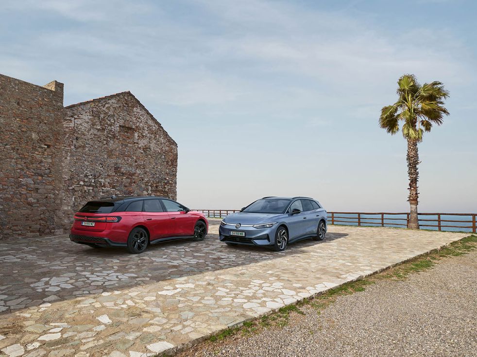 Ein roter VW ID.7 GTX Tourer und ein blauer VW ID.7 Tourer stehen auf einer Parkfläche am Meer.