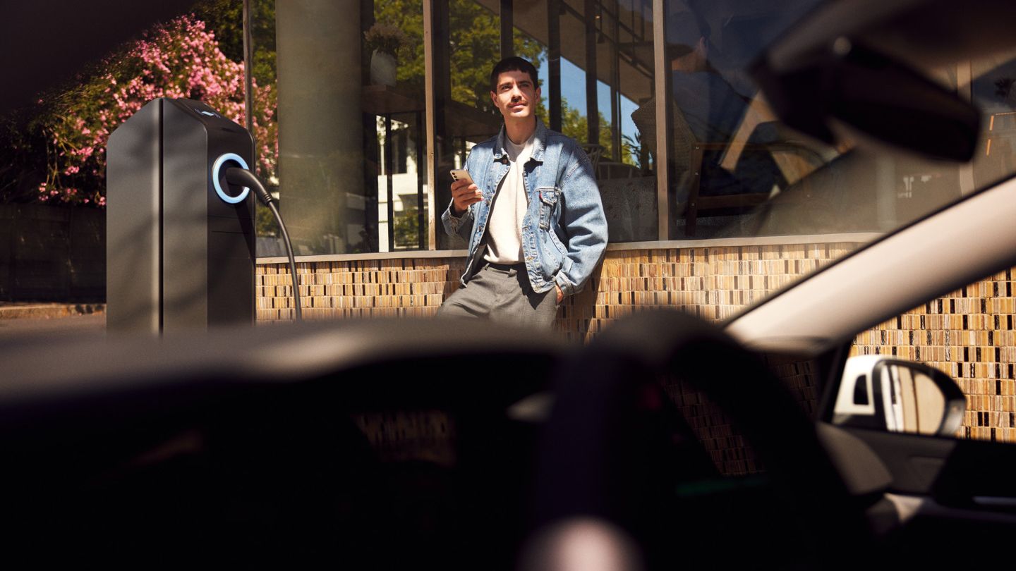 Blick durch die Windschutzscheibe eines Golf auf einen Mann, der neben einer Ladesäule steht. 