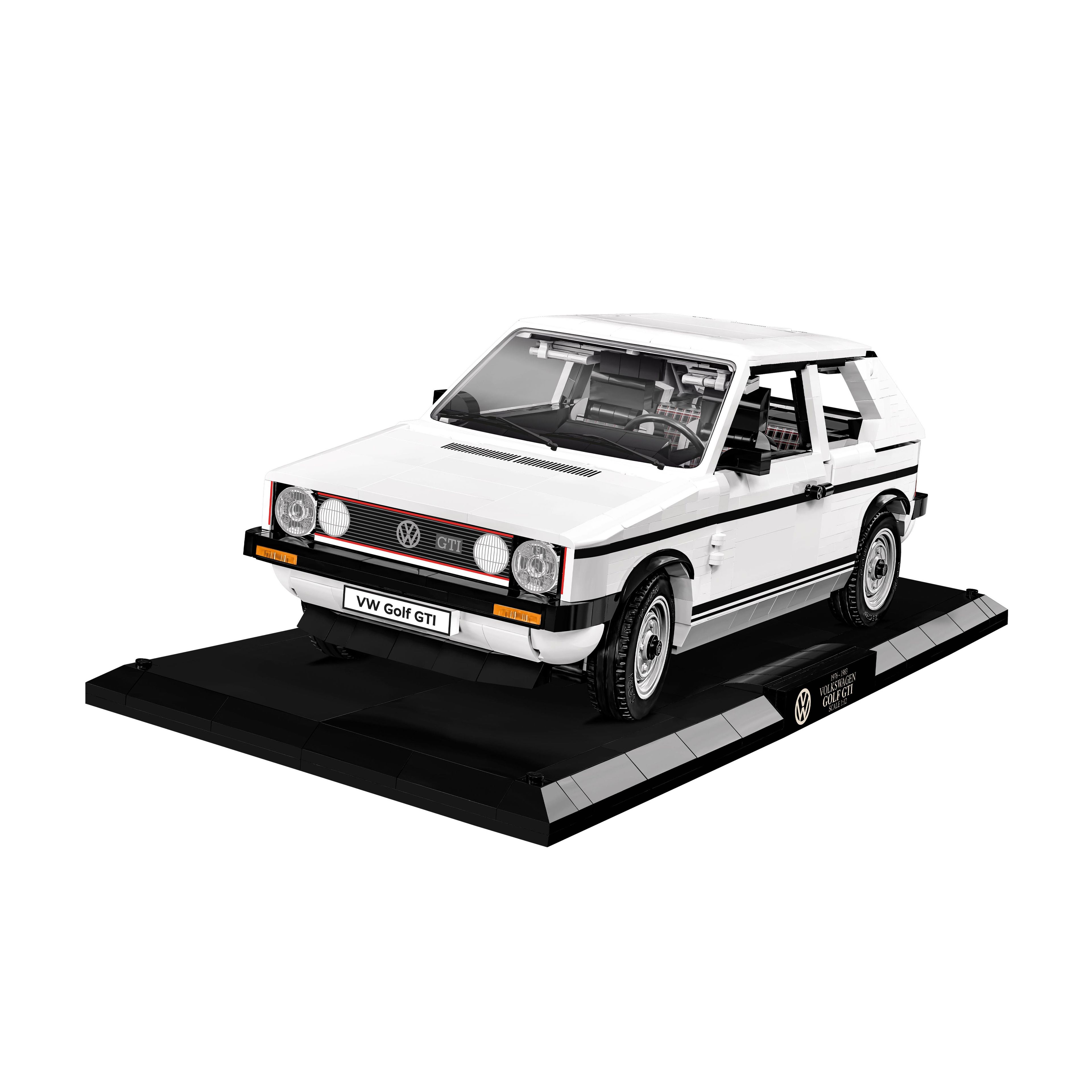 Das Bild zeigt einen Bausatz eines weißen VW Golf GTI auf einem Präsentationsständer. Das Auto hat einen klassischen, kantigen Look. Die Frontscheinwerfer und das VW-Emblem sind deutlich sichtbar.