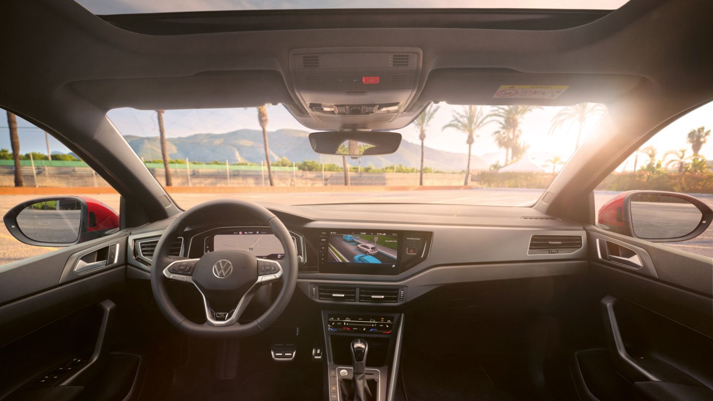 Blick auf das Cockpit mit Lenkrad und Infotainment-System im VW Taigo. Vor dem Fahrzeug sind Palmen und Berge.