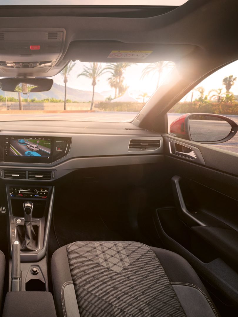 Blick auf das Cockpit mit Lenkrad und Infotainment-System im VW Taigo. Vor dem Fahrzeug sind Palmen und Berge.