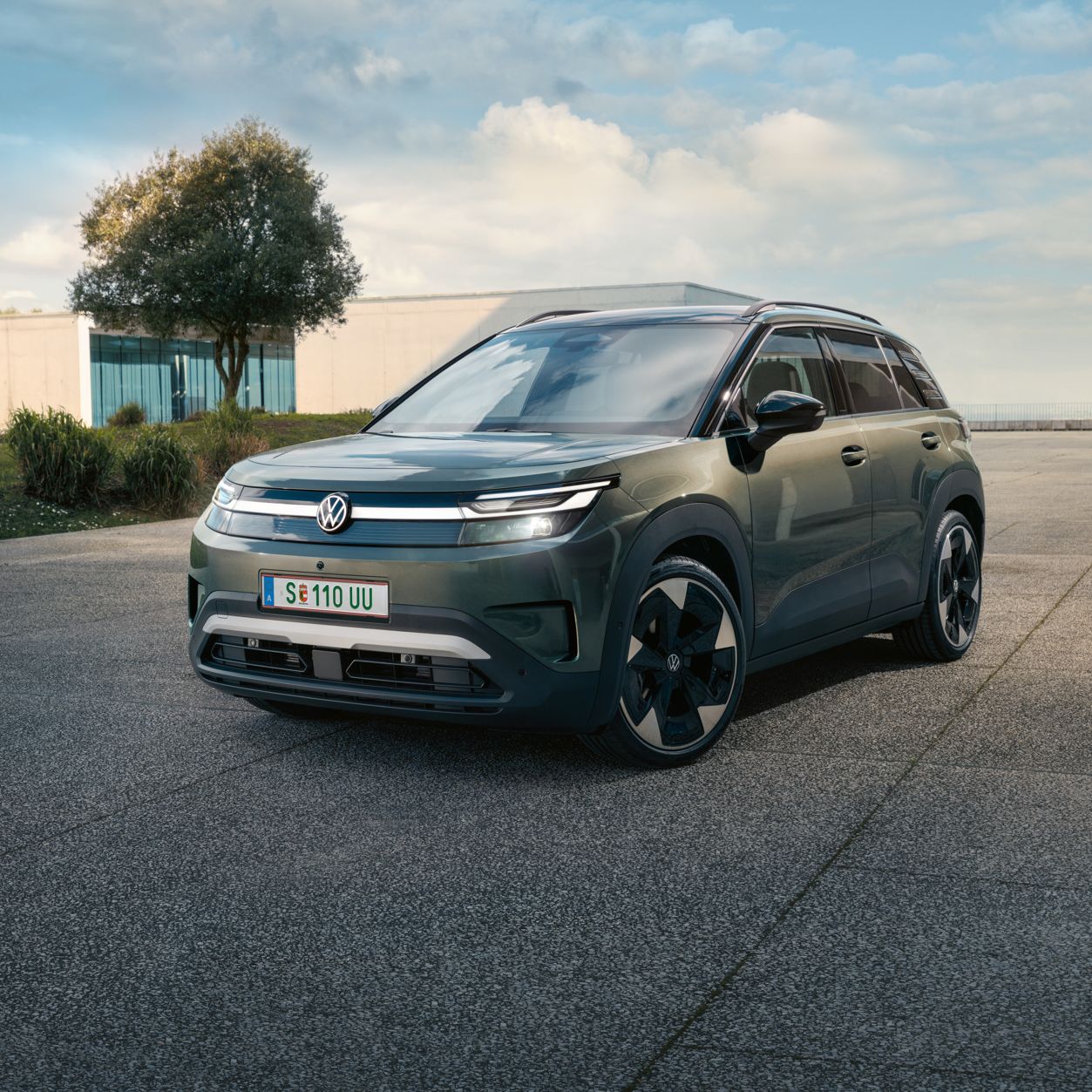 Ein grüner VW ID. Cross steht vor einem modernen Glasgebäude auf einer Betonfläche.