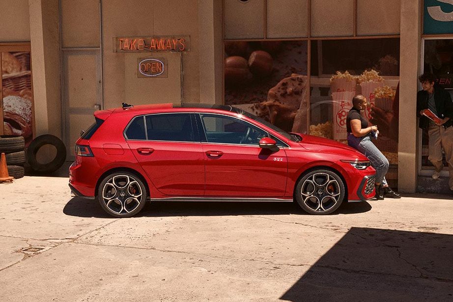 Seitenansicht eines roten VW Golf GTI, Frau lehnt an Motorhaube