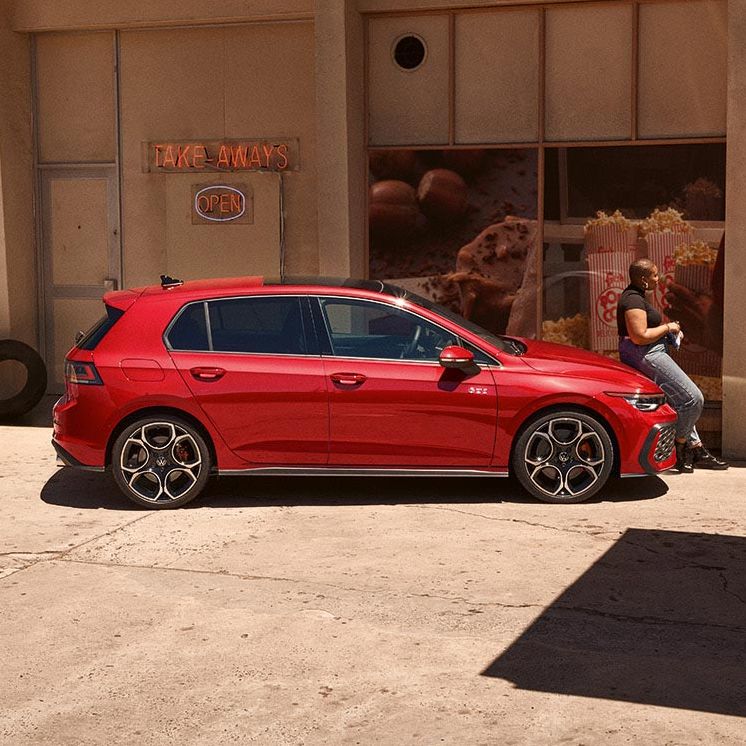 Seitenansicht eines roten VW Golf GTI, Frau lehnt an Motorhaube