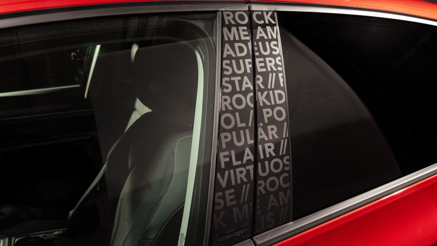 Detailaufnahme der B-Säule eines roten VW Golf Falco Edition. Zu sehen ist dort der Song "Rock me Amadeus", sowie die Worte Superstar, Rockidol, Flair & Virtuose.
