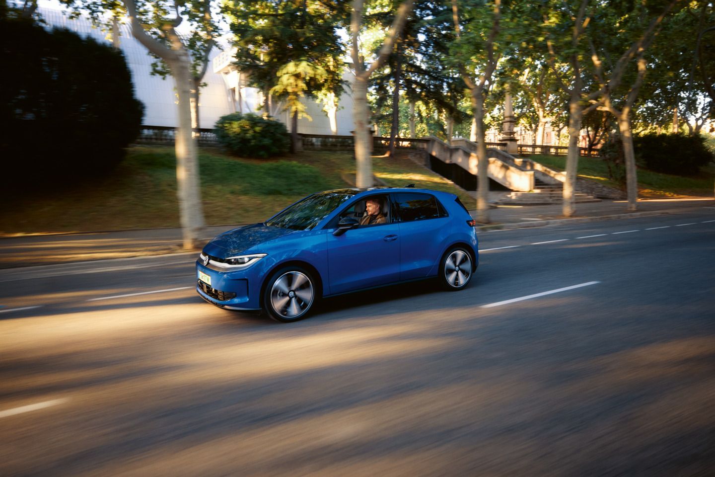 Ein blauer VW ID. Polo fährt auf einer Straße, im Hintergrund eine Reihe Bäume und Häuser.
