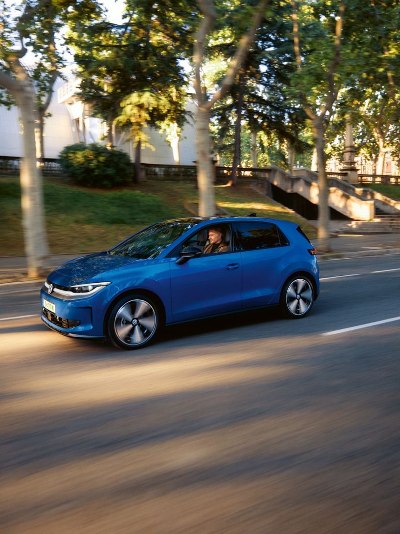 Ein blauer VW ID. Polo fährt auf einer Straße, im Hintergrund eine Reihe Bäume und Häuser.
