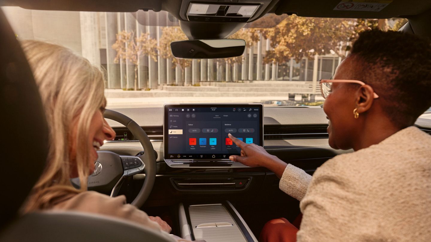 Zwei Frauen, die lachen, sitzen auf den Vordersitzen im VW ID.7 und bedienen das Infotainment-System.