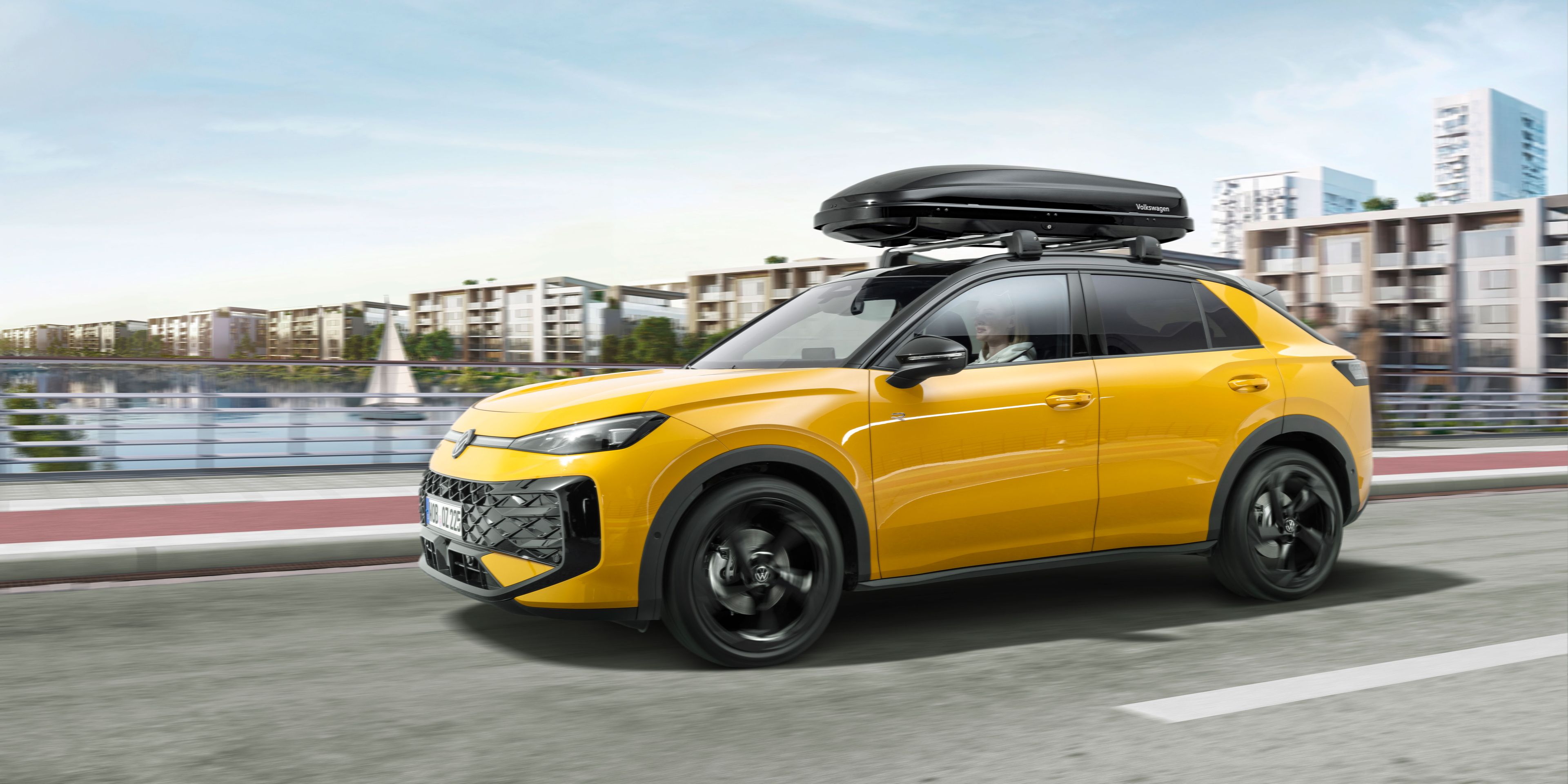 Ein gelber T-Roc mit Dachbox in Fahrt über eine Brücke.