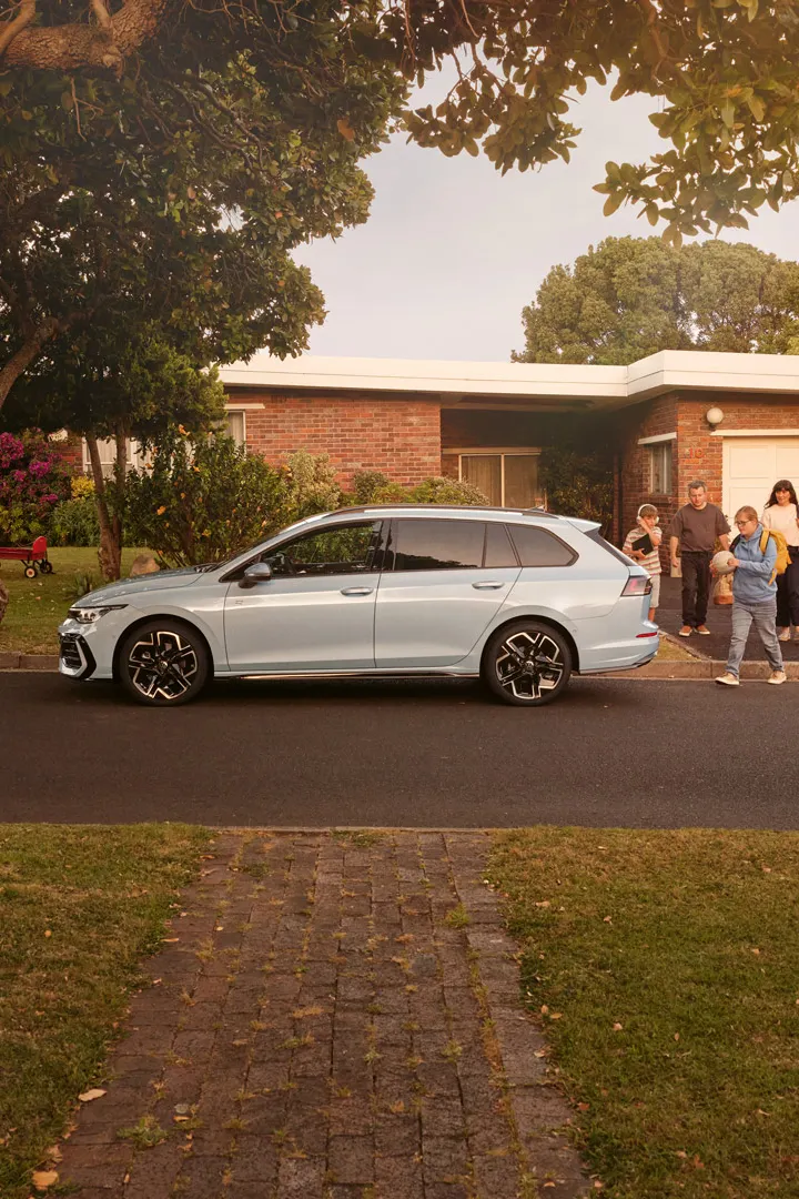 Ein weißer VW Golf Variant parkt vor einem Bungalow in einer Wohnstraße mit Bäumen. 