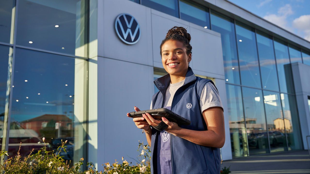 Servicefrau steht mit Tablet vor einem Volkswagen Partner Gebäude.