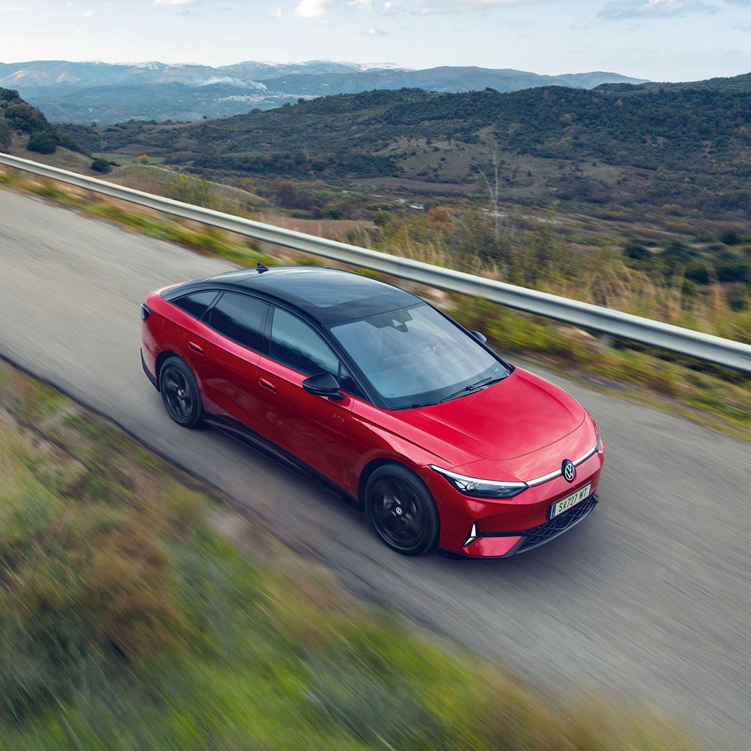 Blick auf die aerodynamisch gestaltete Front eines roten VW ID.7 GTX, der durch eine Berglandschaft fährt.
