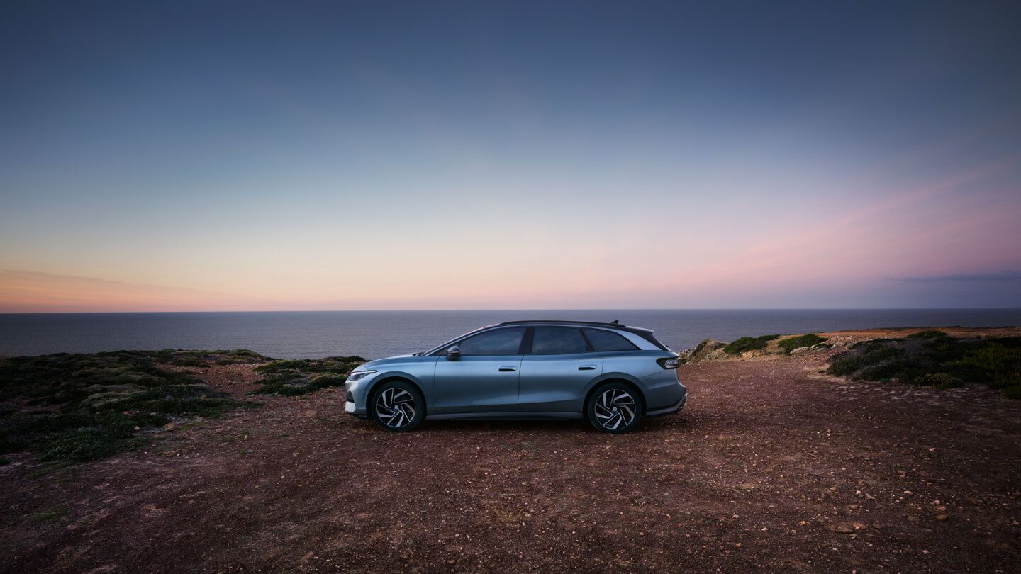 Ein blauer VW ID.7 Tourer steht oben auf einer Klippe im Sonnenuntergang, dahinter das Meer.