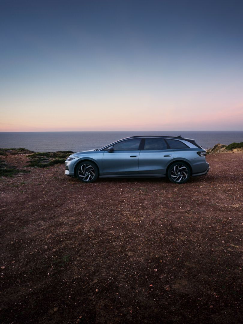 Ein blauer VW ID.7 Tourer steht oben auf einer Klippe im Sonnenuntergang, dahinter das Meer.