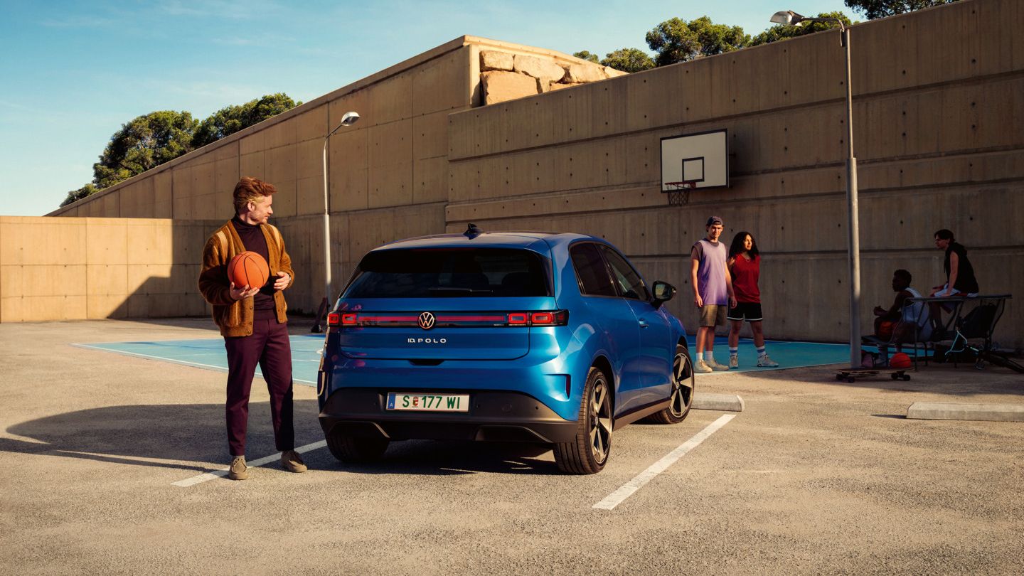 Ein blauer VW ID. Polo parkt vor einem Basketballplatz, daneben steht ein Mann mit Basketball in der Hand.