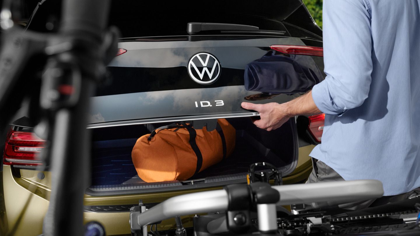 Eine Person lädt Gepäck in den Kofferraum eines ID.3 mit Fahrradträger