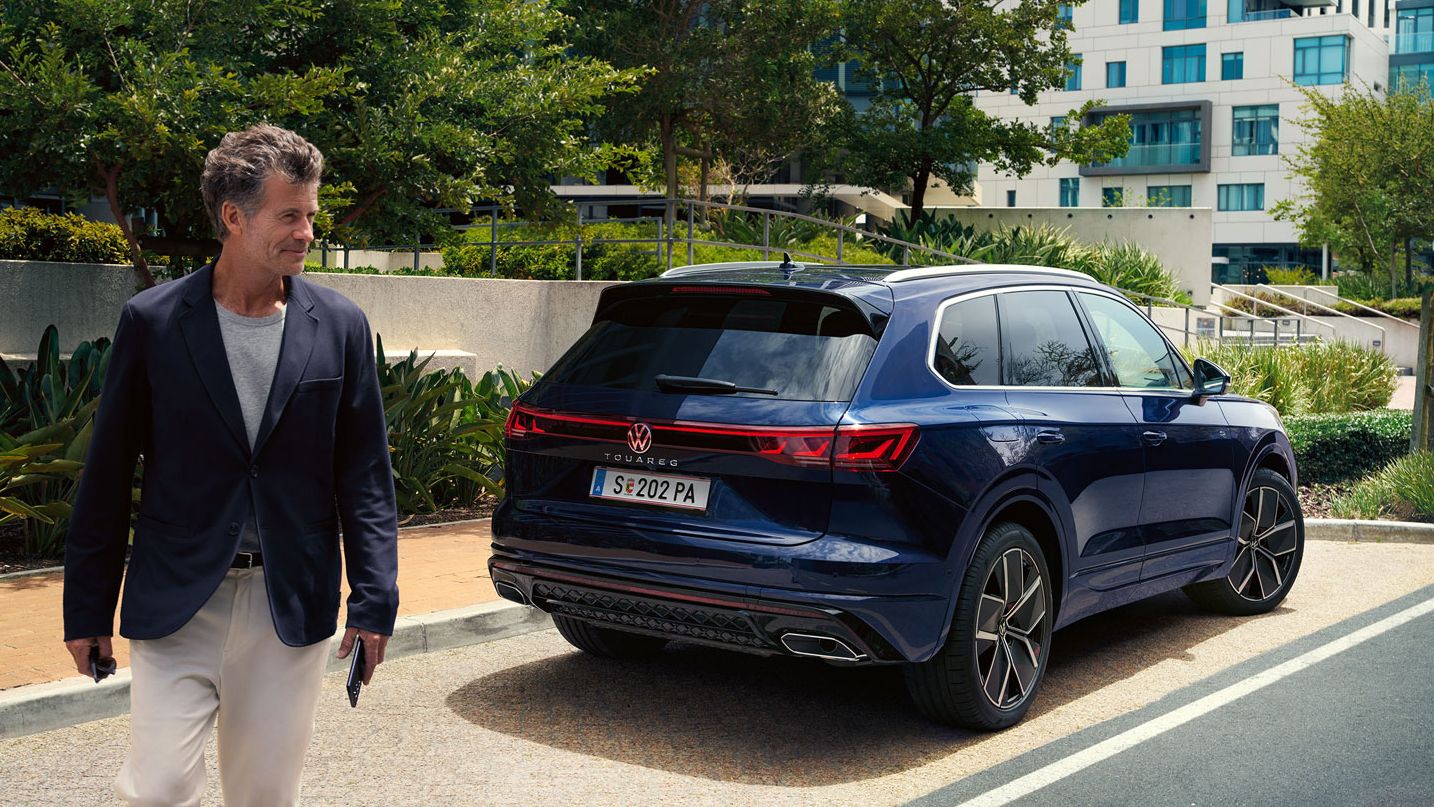 Ein Mann überquert die Straße, schräg hinter ihm ein am Straßenrand parkender VW Touareg R-Line.