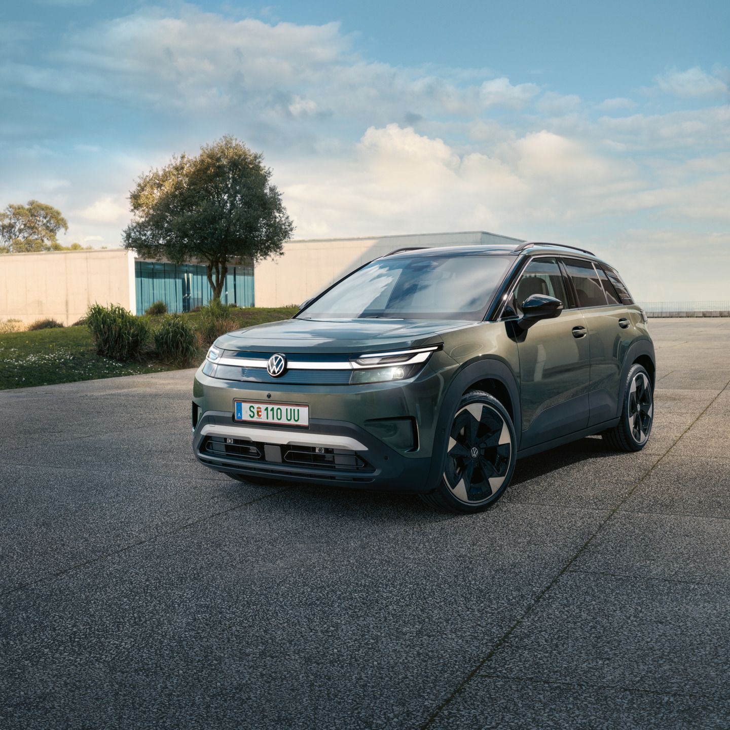 Ein grüner VW ID. Cross steht vor einem modernen Glasgebäude auf einer Betonfläche.