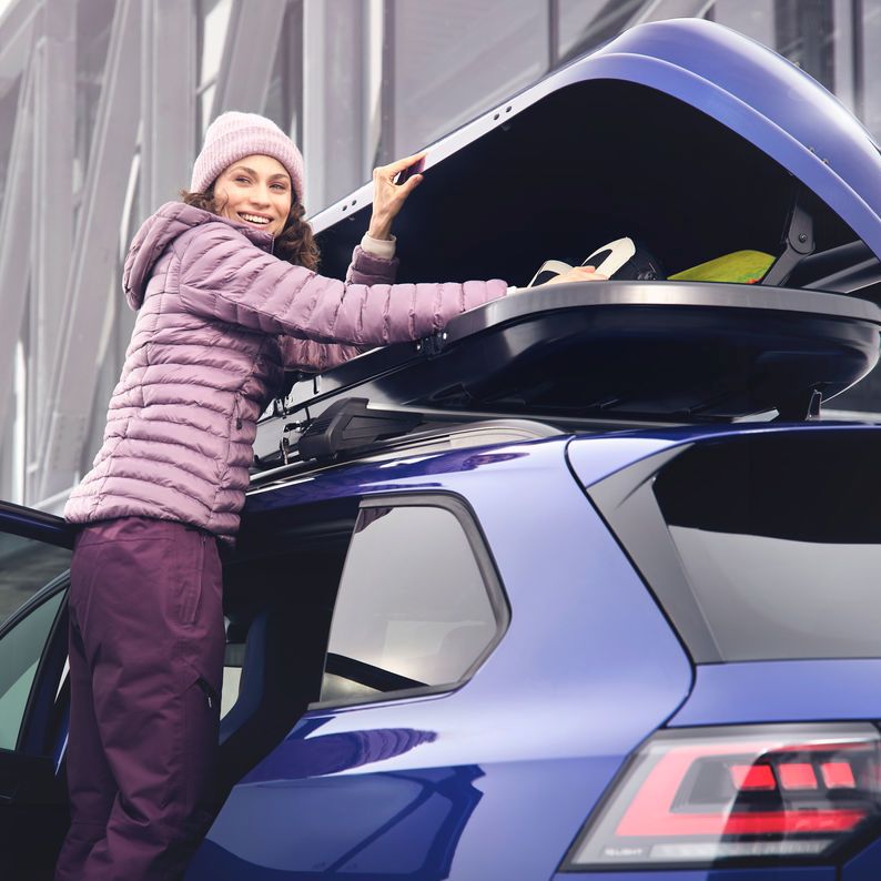 Eine Frau öffnet eine auf einem blauen Volkswagen befestigte Dachbox.