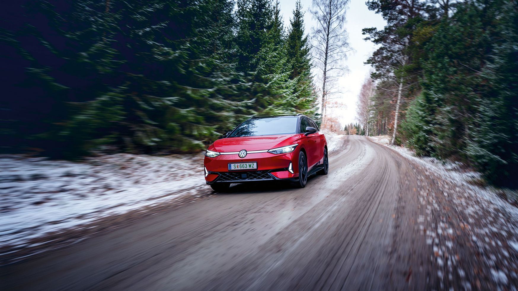 Ein roter VW ID.7 GTX Tourer fährt auf einem Waldweg, auf dem Boden liegt Schnee.