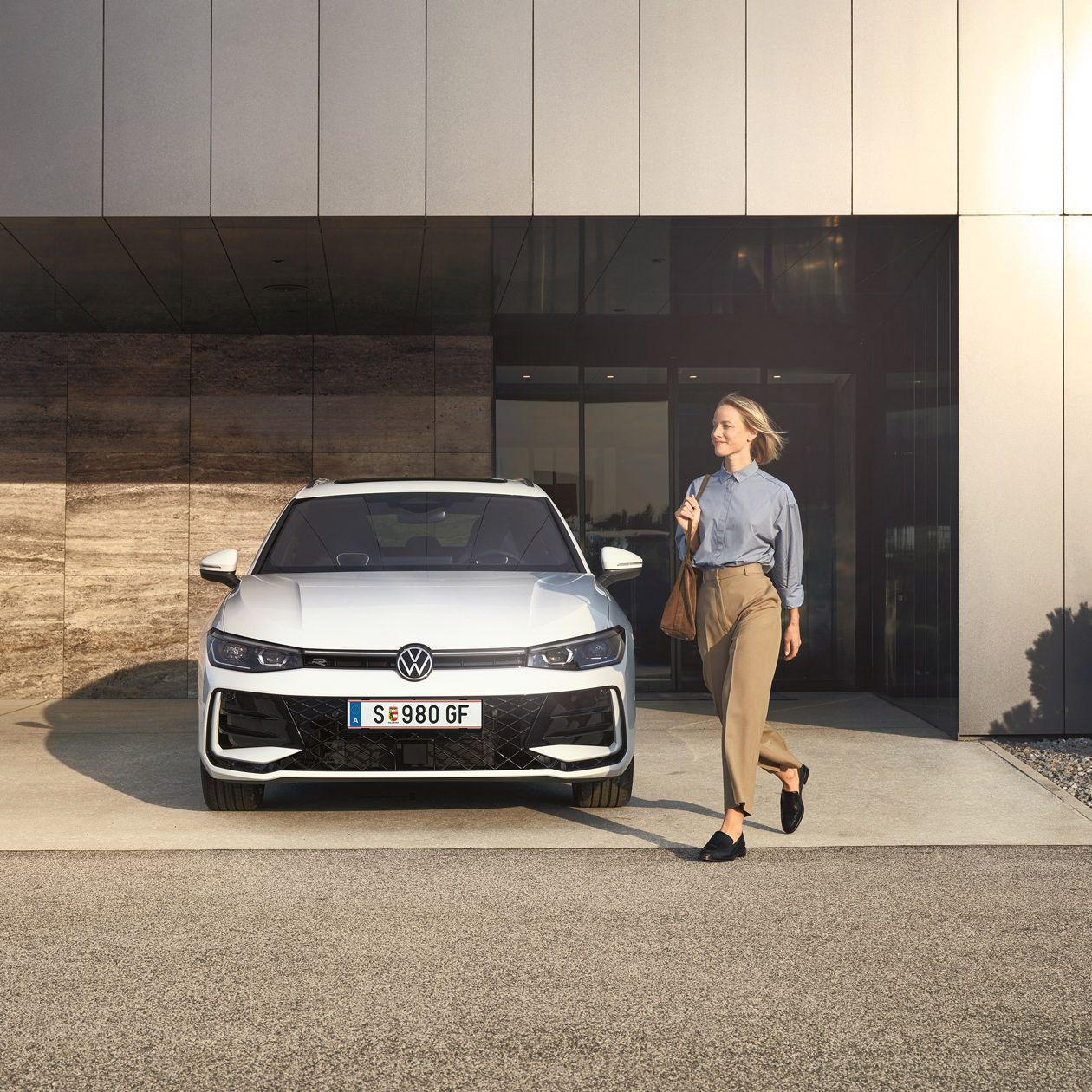 Frontansicht eines weißen VW Passat R-Line, eine Frau geht an ihm vorbei.