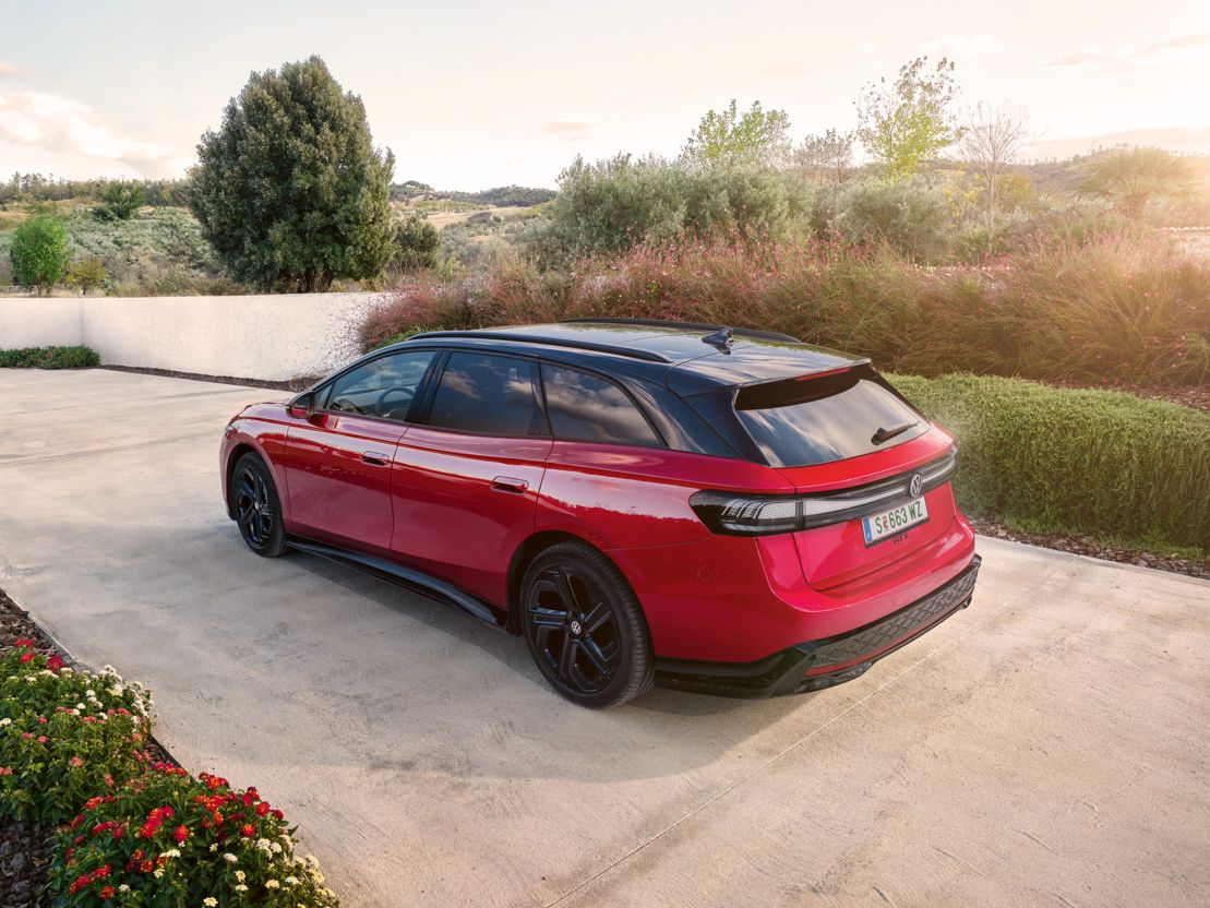 Ein roter VW ID.7 GTX Tourer parkt in einer Auffahrt mit Bäumen im Hintergrund.