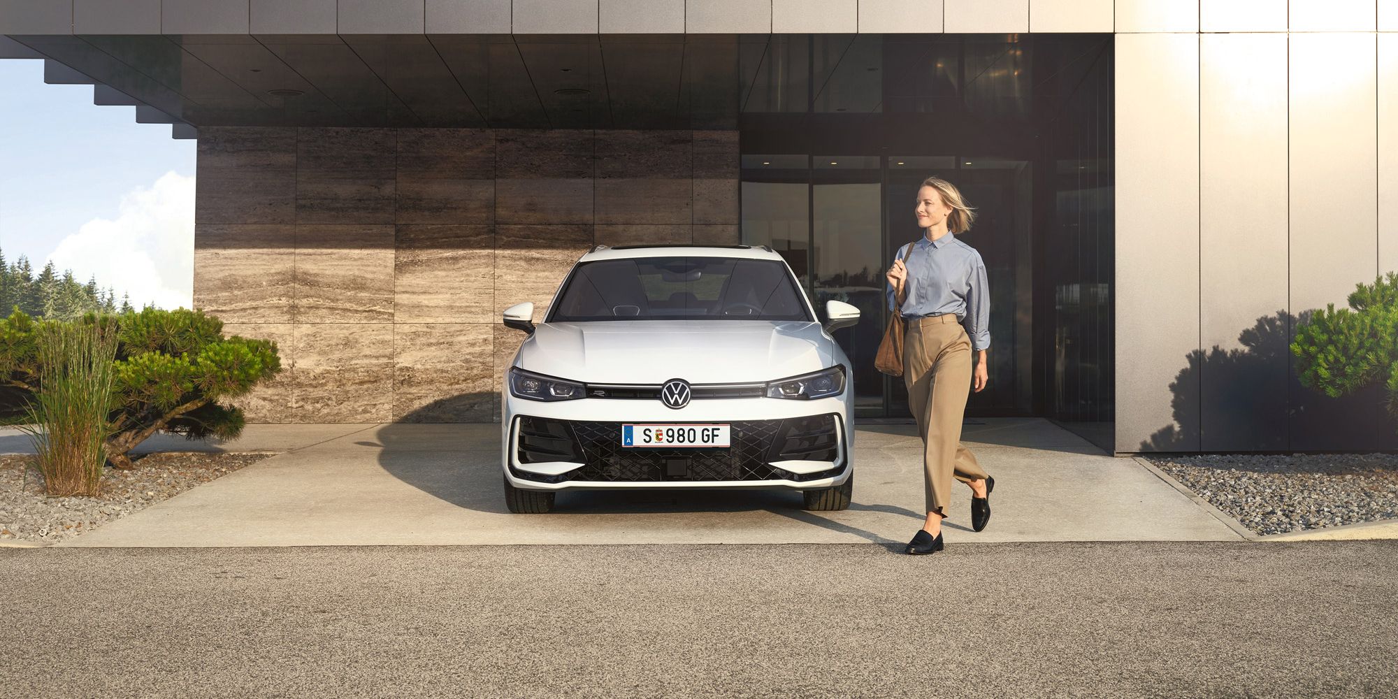 Frontansicht eines weißen VW Passat R-Line, eine Frau geht an ihm vorbei.
