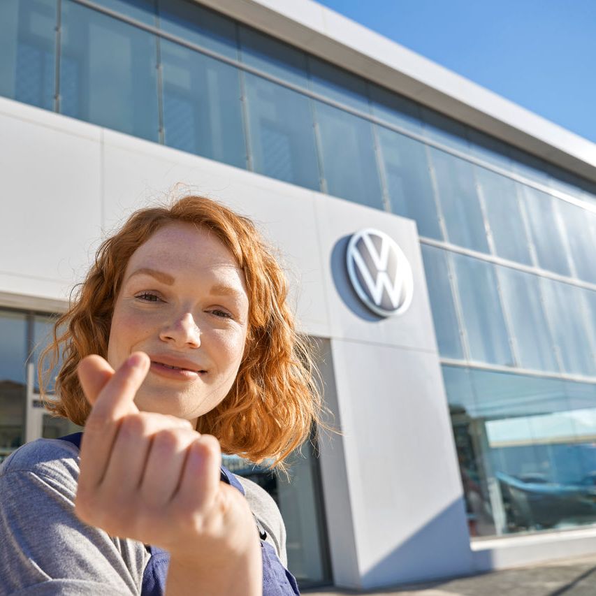 Volkswagen Service Mitarbeiterin vor dem Eingang zu einem Volkswagen Service Partner