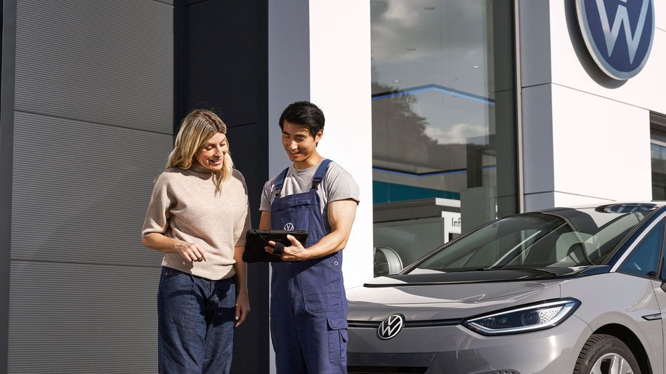 Ein Volkswagen Techniker und eine Kundin stehen vor einem grauen Volkswagen ID.3