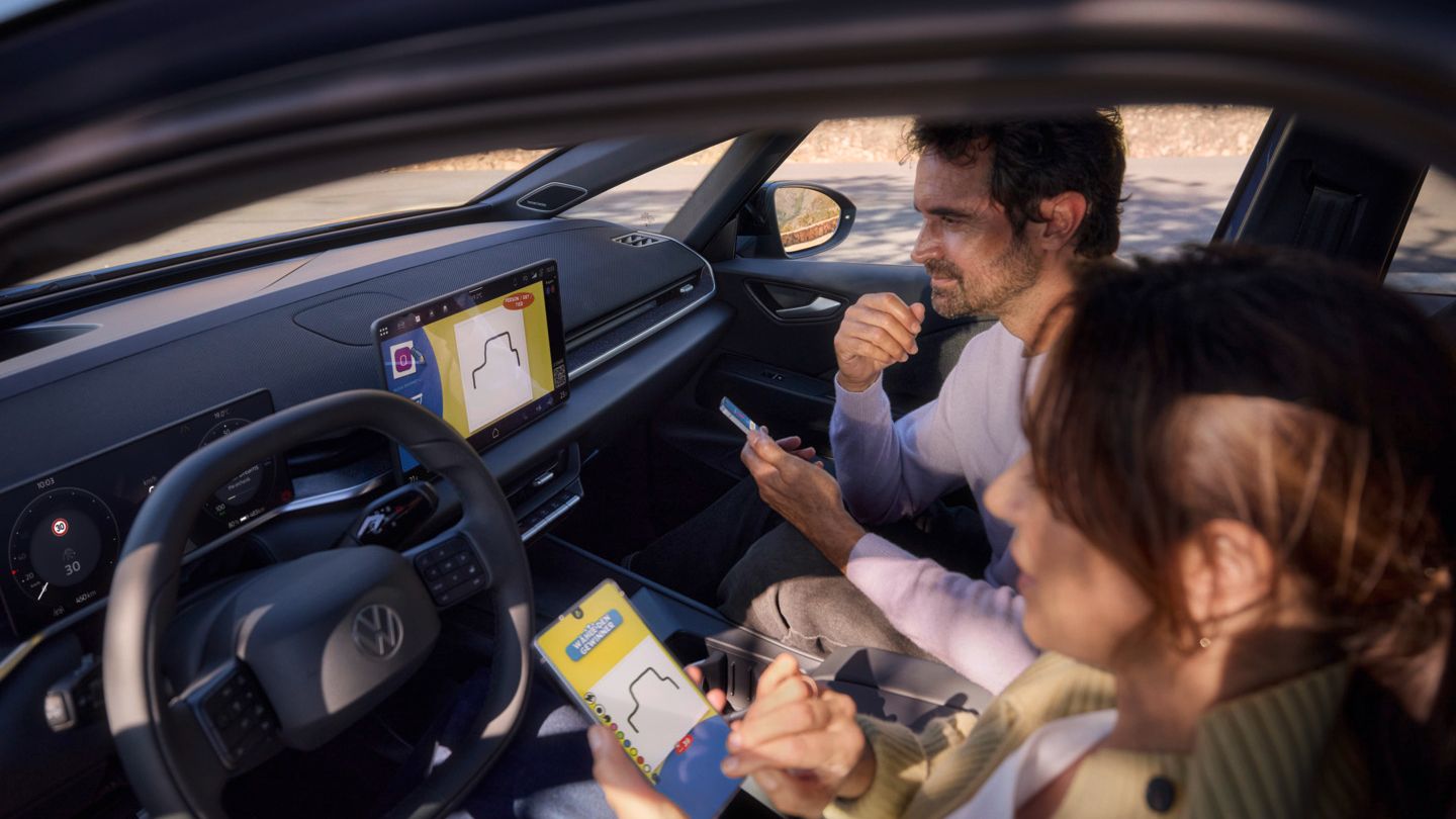 Eine Frau und ein Mann spielen Pictionary auf dem Center-Display eins VW ID.3 Neo und nutzen ihre Smartphones als Controller