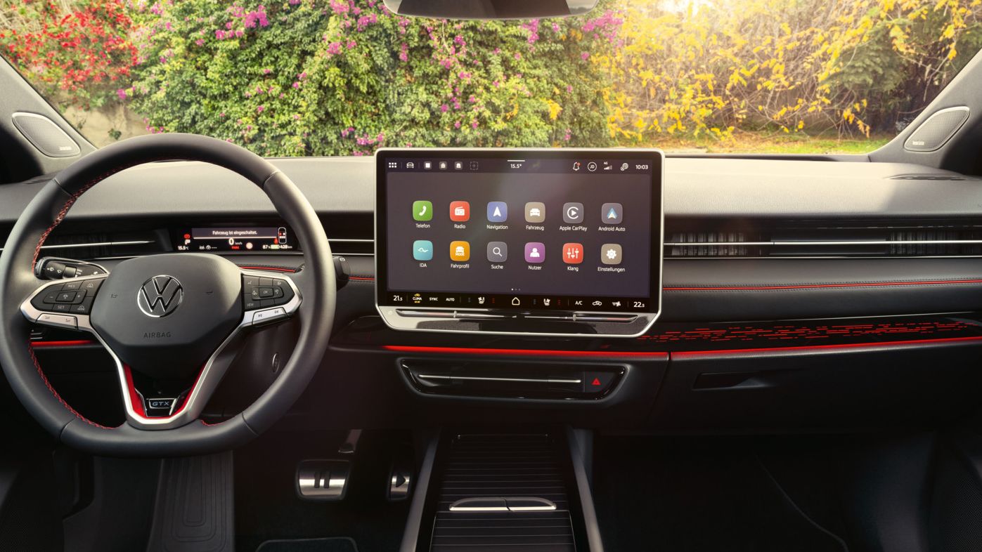 Interieur des ID.7 GTX mit roter Ambientebeleuchtung, roten Ziernähten am Multifunktionslenkrad und dem Infotainmentsystem. 