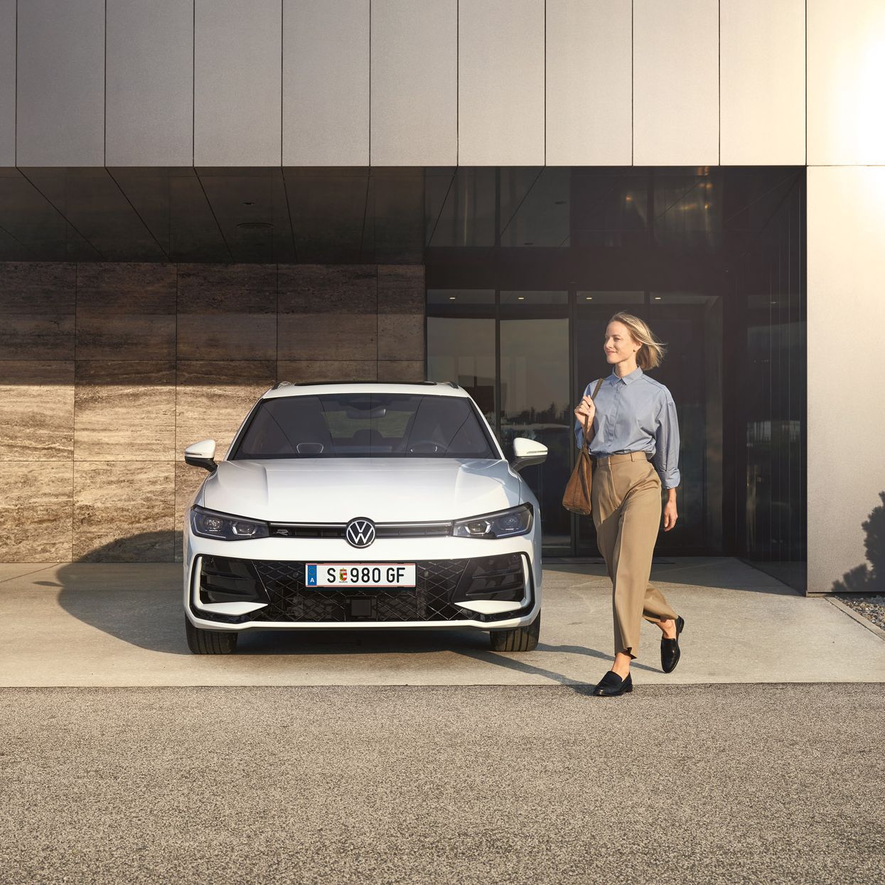 Frontansicht eines weißen VW Passat R-Line, eine Frau geht an ihm vorbei.