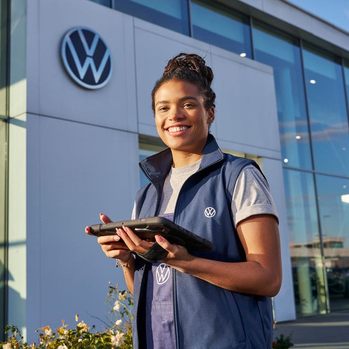 Servicefrau steht mit Tablet vor einem Volkswagen Partner Gebäude.