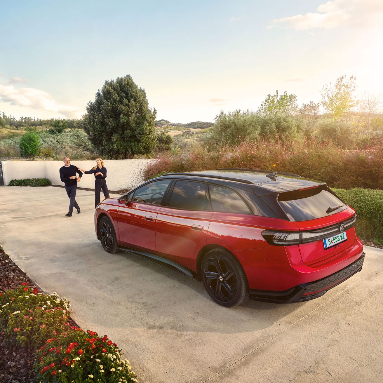 Ein roter VW ID.7 GTX Tourer parkt in einer langen Auffahrt, ein Mann und eine Frau wollen einsteigen.